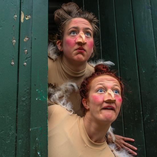 To kvinder klædt ud som høns kigger ud af en døråbning. 