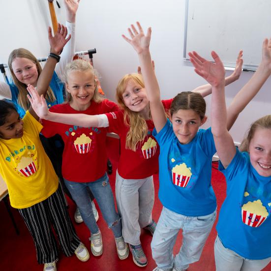 Børn i blå t-shirts med popcornbægre på ser glade ud og rækker hænderne i vejret 
