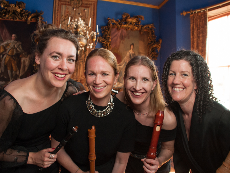 Fire smilende og velklædte kvinder i barokke omgivelser med blokfløjter. 