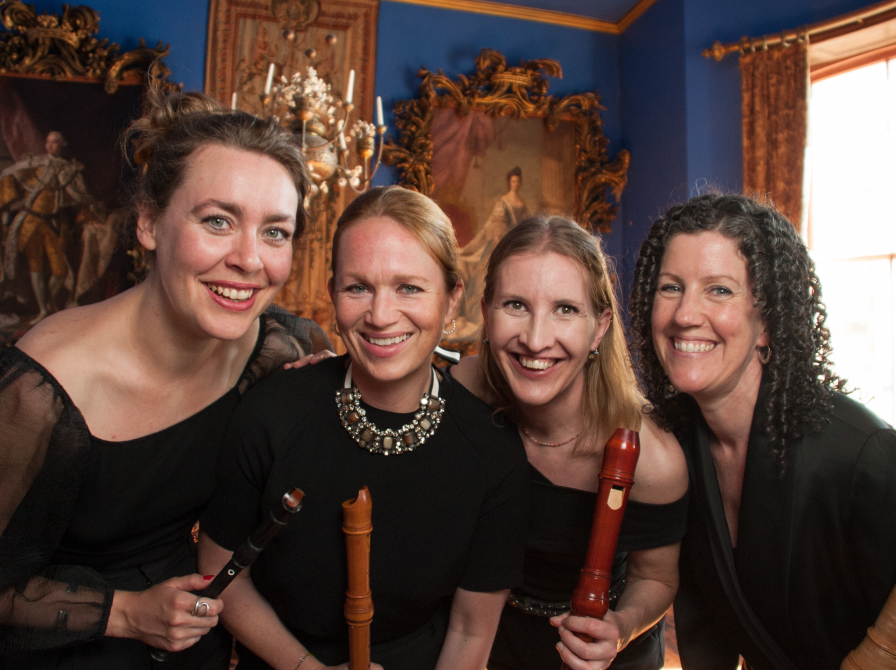 Fire smilende og velklædte kvinder i barokke omgivelser med blokfløjter. 